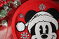 Red plate with a black and white design of a character wearing a Santa hat, surrounded by Christmas decorations.